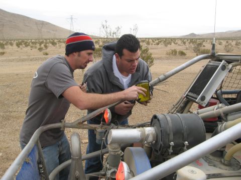 1986 Ford Bronco - Two men inspect the engine of a dune buggy in a desert setting, with power lines visible in the background.