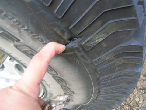 1986 Ford Bronco - A finger points to a damaged section of a tire tread, revealing the wear and tear on the rubber.