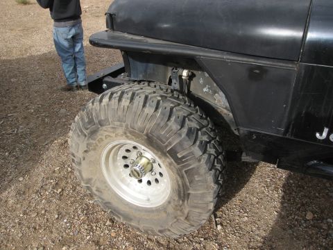 1986 Ford Bronco - A black Jeep Wrangler with large off-road tires is shown from the front quarter angle.