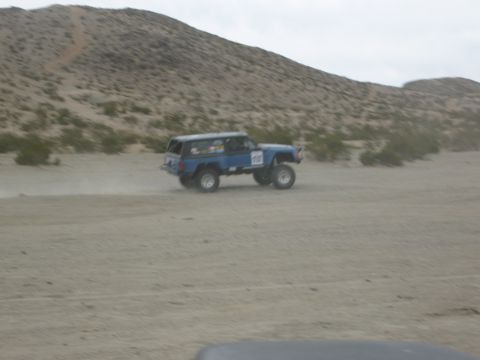 1986 Ford Bronco - Modified blue SUV kicks up dust while driving off-road in a desert environment.