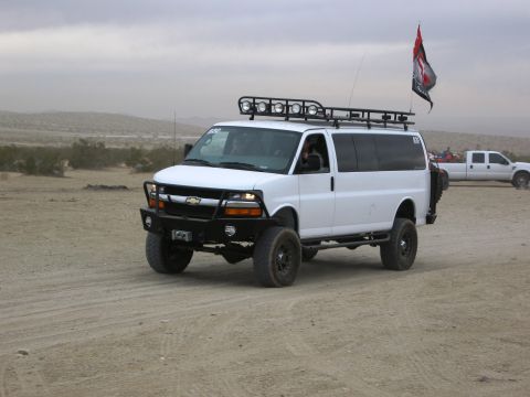 1986 Ford Bronco - Modified white van with off-road accessories in a desert setting, with another truck in the distance.