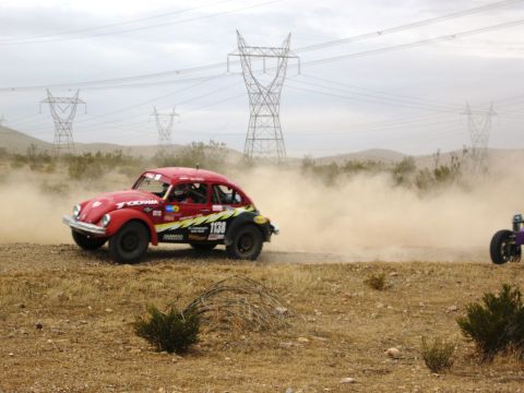 1986 Ford Bronco - A red off-road Volkswagen Beetle races through a dusty desert landscape with power lines overhead.