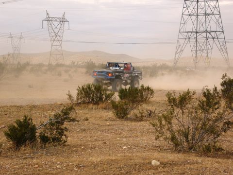 1986 Ford Bronco - Custom off-road truck navigates a dusty desert terrain under a hazy sky.
