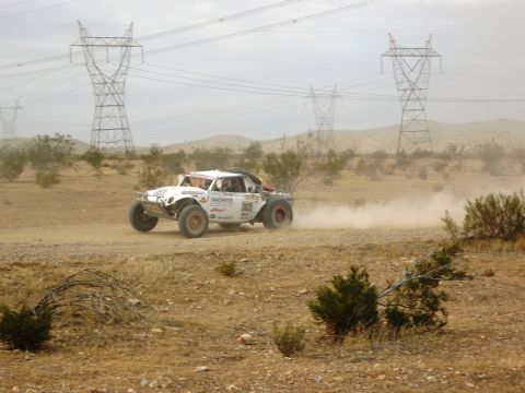 1986 Ford Bronco - An off-road race truck navigates a dusty desert terrain under a cloudy sky.