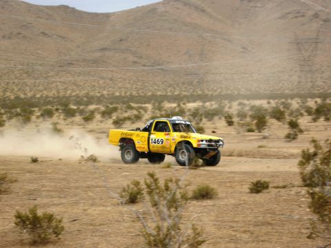 1986 Ford Bronco - Off-road truck races through a dusty desert landscape.