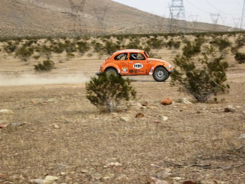 1986 Ford Bronco - An orange Volkswagen Beetle rally car navigates a dusty desert terrain, displaying the number 1191 on its side.