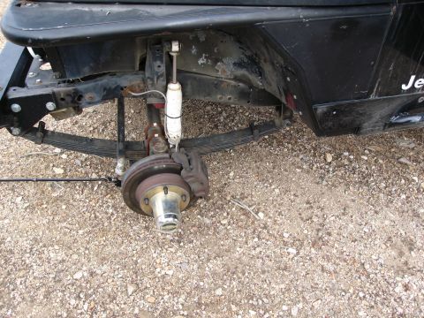 1986 Ford Bronco - Close-up of the front suspension and fender area of a Jeep, showing leaf springs and a shock absorber.