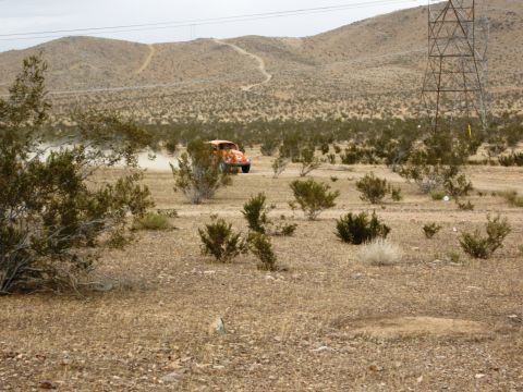 1986 Ford Bronco - Orange VW Beetle Baja Bug kicks up dust while driving through a desert landscape.
