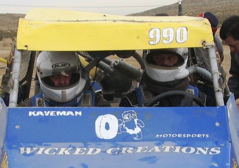 1986 Ford Bronco - Two drivers in a custom off-road buggy, identified as 'Wicked Creations', are ready for the race with the number 990 displayed.
