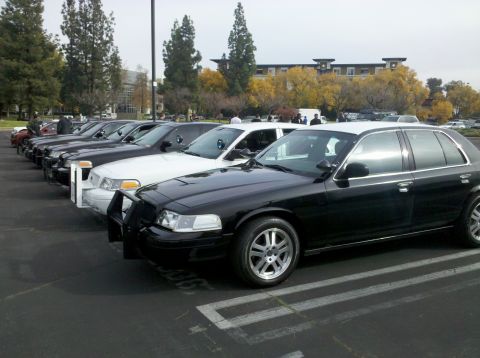 2004 Ford Crown Victoria - A line of black and white Ford Crown Victoria police cars are parked in a lot.