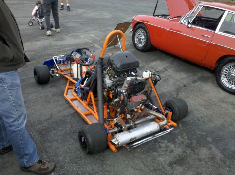 2004 Ford Crown Victoria - A custom go-kart and a red classic sports car are parked side-by-side on pavement.