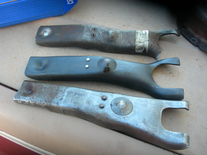 Three metal clutch fork parts laid out on a surface. One has a sticker with numbers
