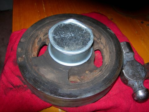 1984 Ford Bronco - A crankshaft pulley shows damage to its center hub, with a hammer nearby.