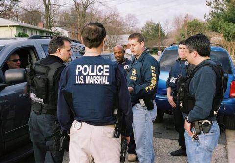 1991 Ford LTD Crown Victoria - Law enforcement officers are seen in a huddle near parked vehicles on a residential street.