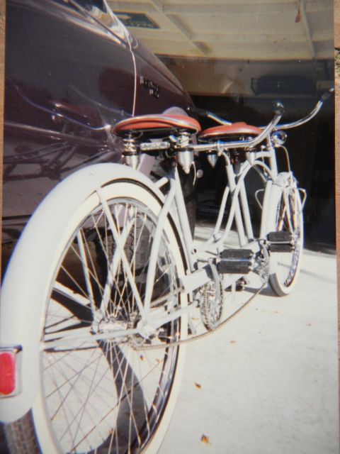 1997 Ford Ranger - A tandem bicycle with white frame and red seats is parked next to a dark vehicle.