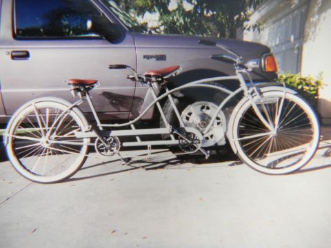 1997 Ford Ranger - A white tandem beach-cruiser bicycle with brown saddles and whitewall tires poses on a driveway in front of a mauve/purple Ford Ranger exte…