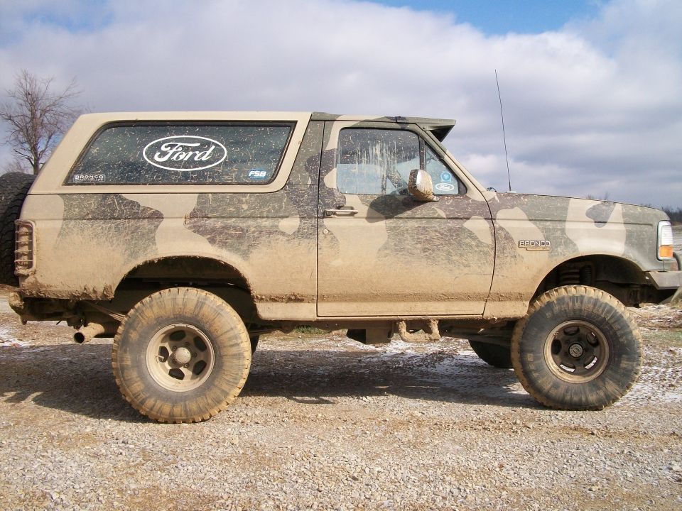 Muddy 1995 Ford Bronco with camo paint and big tires, parked on a dirt road
