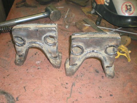 1995 Ford Bronco - Two custom-welded metal brackets are shown on a workbench, alongside various tools and equipment.