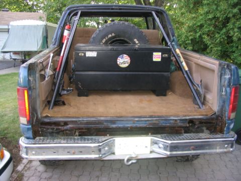 1986 Ford Bronco - Rear view of a blue Ford Bronco, showing its cargo area equipped with a toolbox and spare tire.