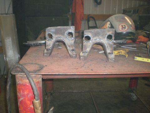 1995 Ford Bronco - Two custom-welded metal brackets sit on a workbench next to welding equipment.