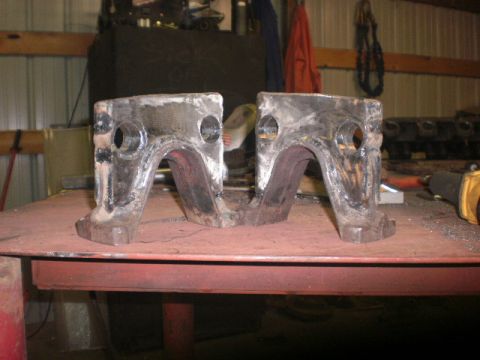 1995 Ford Bronco - Two heavy-duty metal brackets sit on a workbench in a garage setting.