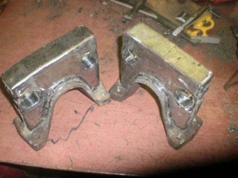 1995 Ford Bronco - Two metal brackets with bolts and yellow padding are shown on a workbench.
