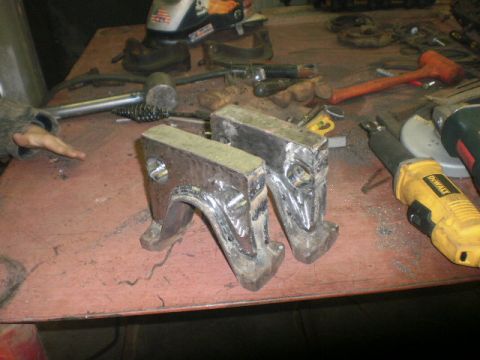 1995 Ford Bronco - Two custom metal brackets sit on a workbench surrounded by tools, suggesting a fabrication or repair project.