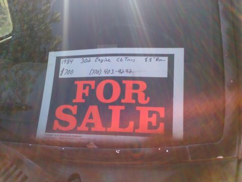 1990 Ford Bronco - A 'For Sale' sign is displayed on the windshield of a vehicle, listing its year, engine, transmission, price, and contact information.