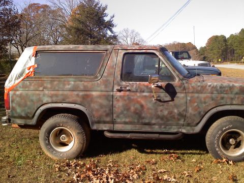 1990 Ford Bronco - Side view of a Ford Bronco painted in camouflage. A second vehicle is visible in the background.
