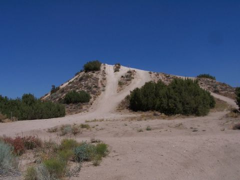 1990 Ford Bronco - A steep sandy hill-climb rutted with tire tracks rises from a flat desert staging area, flanked by juniper bushes under a deep blue sky. A…