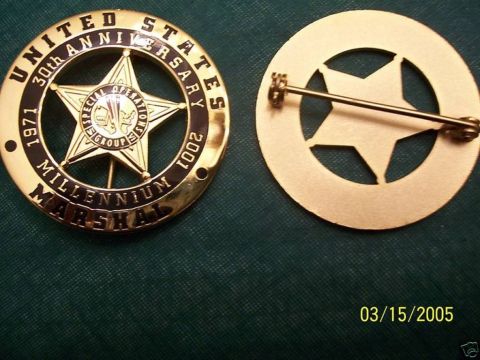 1991 Ford LTD Crown Victoria - Gold-tone circle-star badge shown face-up and face-down on dark green fabric, reading "UNITED STATES MARSHAL" and "30th ANNIVERSARY 1971-20…