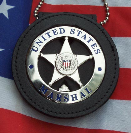 1991 Ford LTD Crown Victoria - A United States Marshal badge in a black leather holder with a beaded neck chain, displayed against an American flag background. The silver…