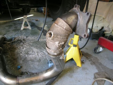 1995 Ford Probe - Close-up of an exhaust pipe section with heat wrap, resting on jack stands in a garage.