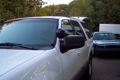 2001 Ford Crown Victoria - A white Ford Expedition is parked next to a blue sedan, with trees and a white trailer in the background.