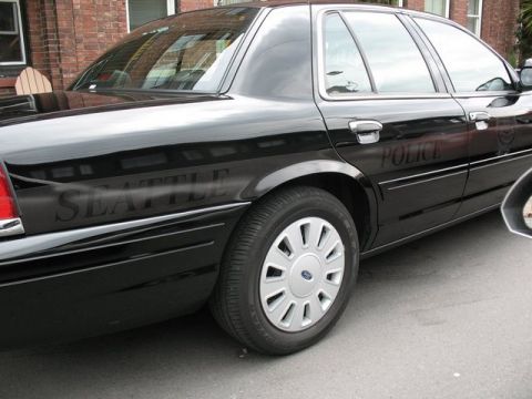 1991 Ford LTD Crown Victoria - A black police car is seen from the side, with 'SEATTLE' and 'POLICE' text visible on its doors.
