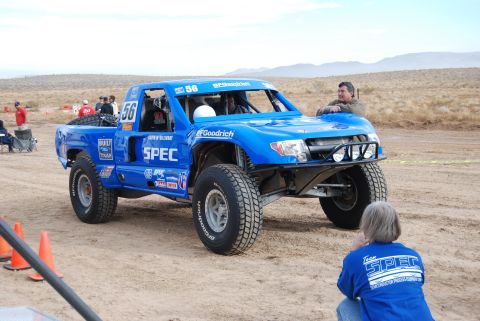 1982 Ford Bronco - A blue off-road racing truck is parked on a dirt track with spectators around.