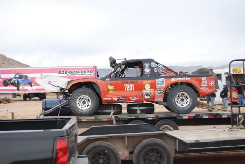 1982 Ford Bronco - Off-road racing truck being transported on a trailer, with other vehicles and a trailer in the background.