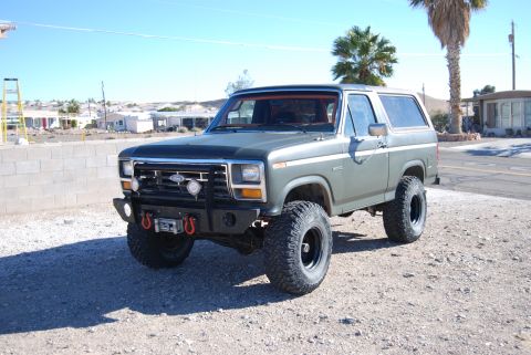 1982 Ford Bronco - This lifted Ford Bronco sits parked on a gravel lot with a desert landscape in the background.