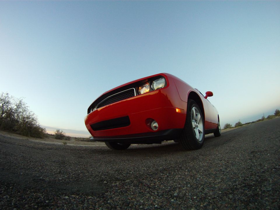 Low ground-level fisheye view of a red Dodge Challenger front-left corner on desert gravel