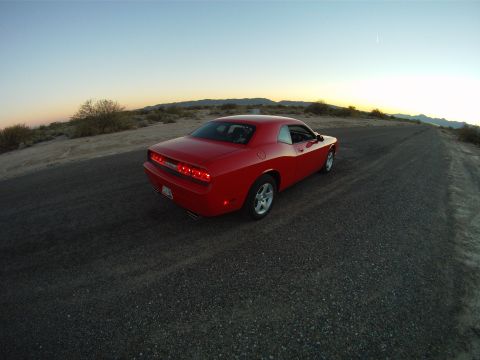 2010 Dodge Challenger - A red Dodge Challenger is seen from a rear quarter angle on a desert road as the sun sets.