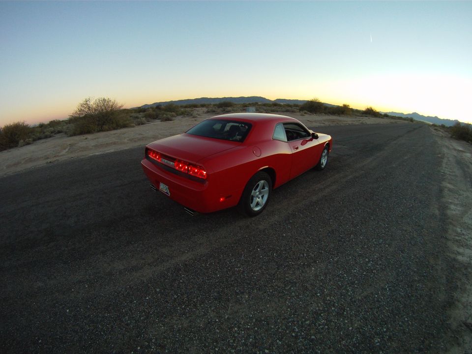 Red Dodge Challenger rear three-quarter on a desert road at dusk, taillights lit