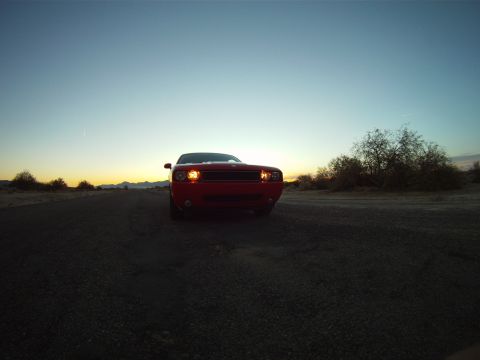 2010 Dodge Challenger - Red Dodge Challenger on a dirt road at dusk with headlights on.