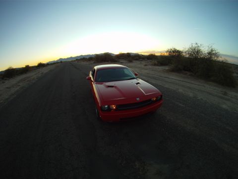2010 Dodge Challenger - A red Dodge Challenger drives down a desert road as the sun sets.