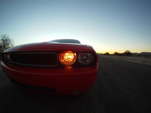 2010 Dodge Challenger - A red Dodge Challenger is captured from a low angle at sunset, highlighting its front corner and illuminated headlight.