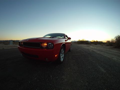 2010 Dodge Challenger - A red Dodge Challenger sits on a desolate dirt road as the sun sets in the background.