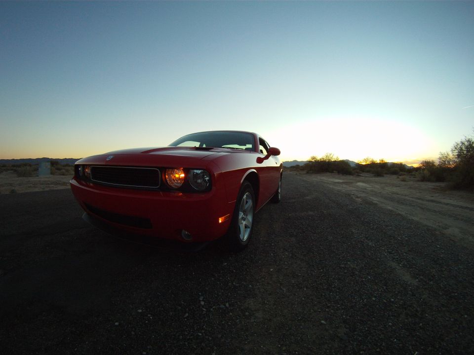 Red Dodge Challenger parked on a dirt road at sunset, front 3/4 view