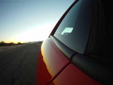 2010 Dodge Challenger - A red car drives down a desert road as the sun sets on the horizon.