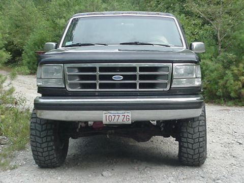 1993 Ford Bronco - Head-on front view of a black Ford Bronco on a gravel trail, showing the bar-style grille with the blue Ford oval, rectangular composite he…