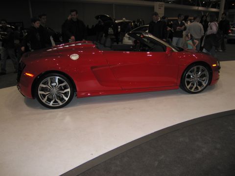 1991 Ford LTD Crown Victoria - A red convertible sports car is displayed indoors with people around.