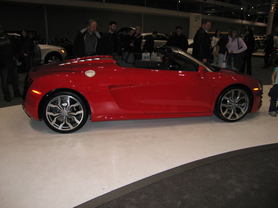 Red convertible sports car side view, black top up, custom wheels, on display